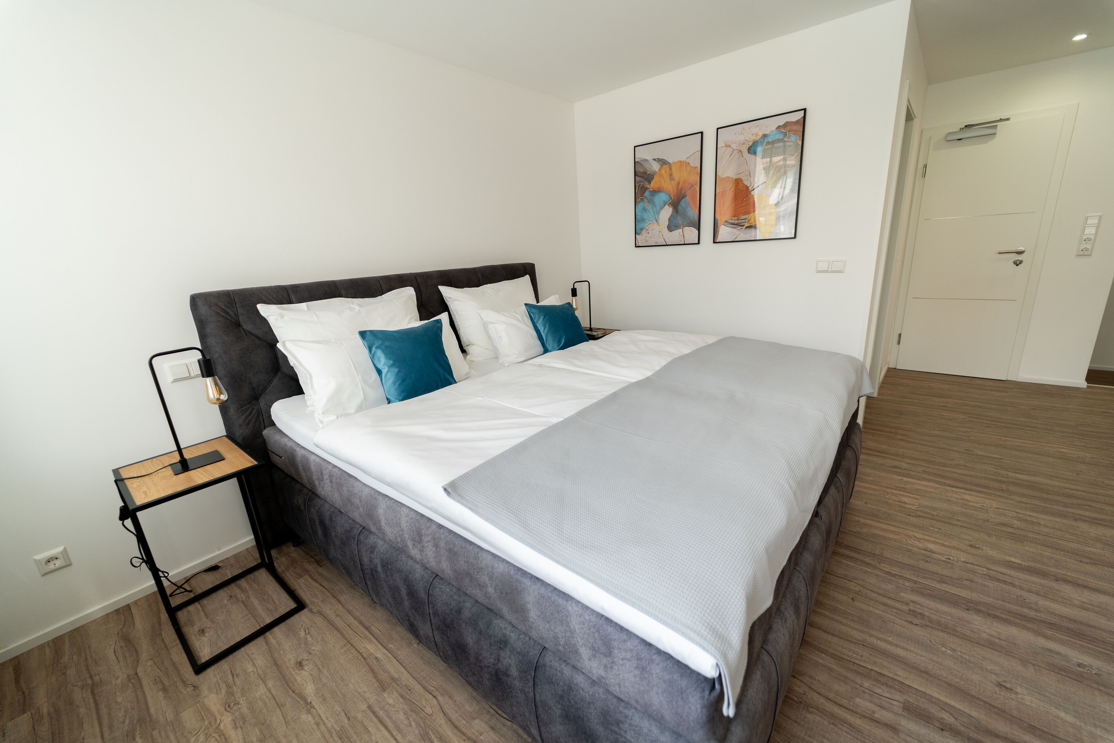 A modern bedroom with a large bed, a bedside table, and two wall-mounted artworks.