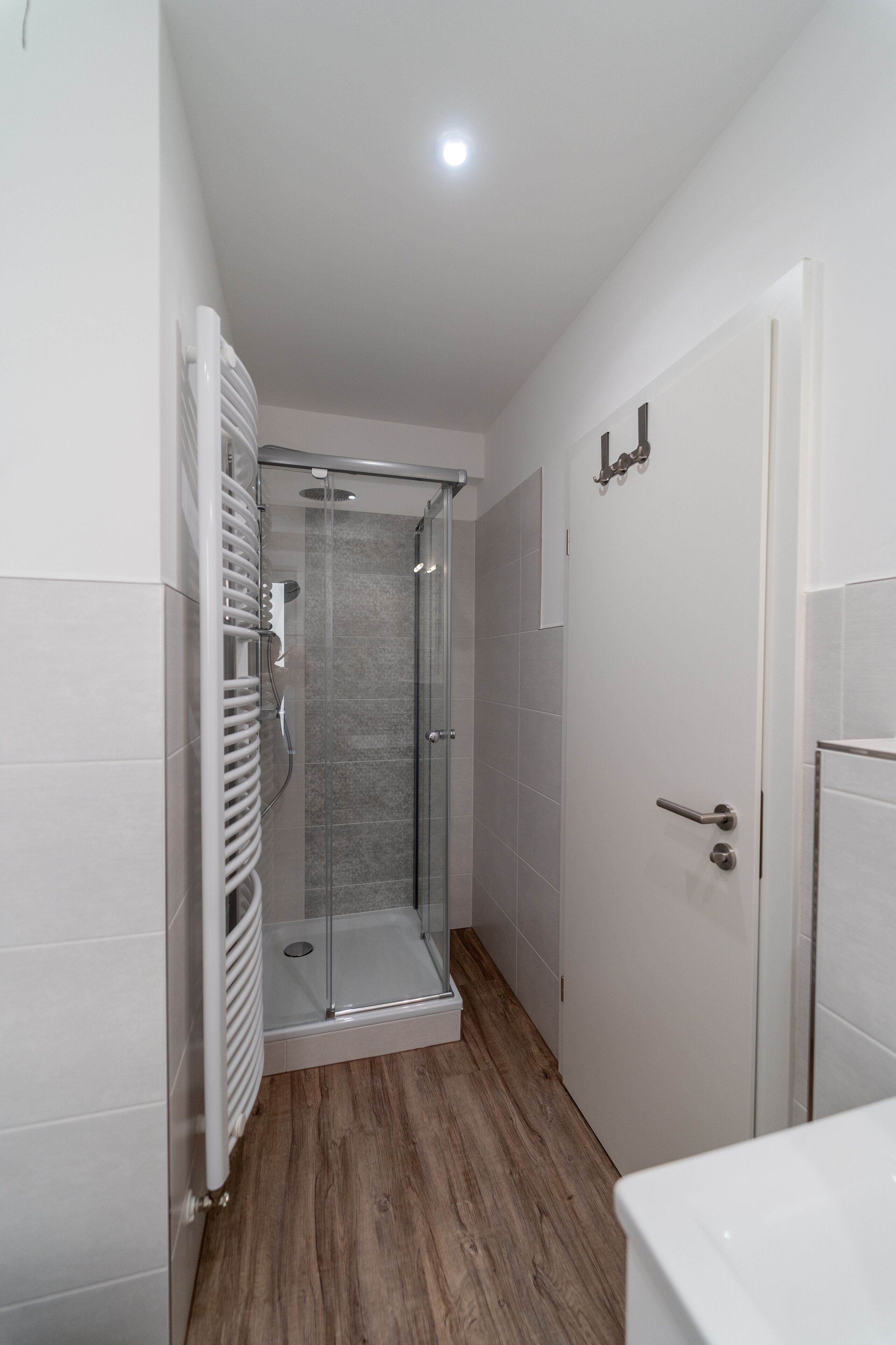 Une petite salle de bain avec une douche en verre, des murs recouverts de carreaux blancs et un plancher en bois.