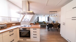 A modern kitchen with white cabinetry, a built-in oven, and a wooden countertop. There is a dining area with a table and chairs, and a kitchen island with a sink. - Apartments am Marktplatz (Bad Urach)