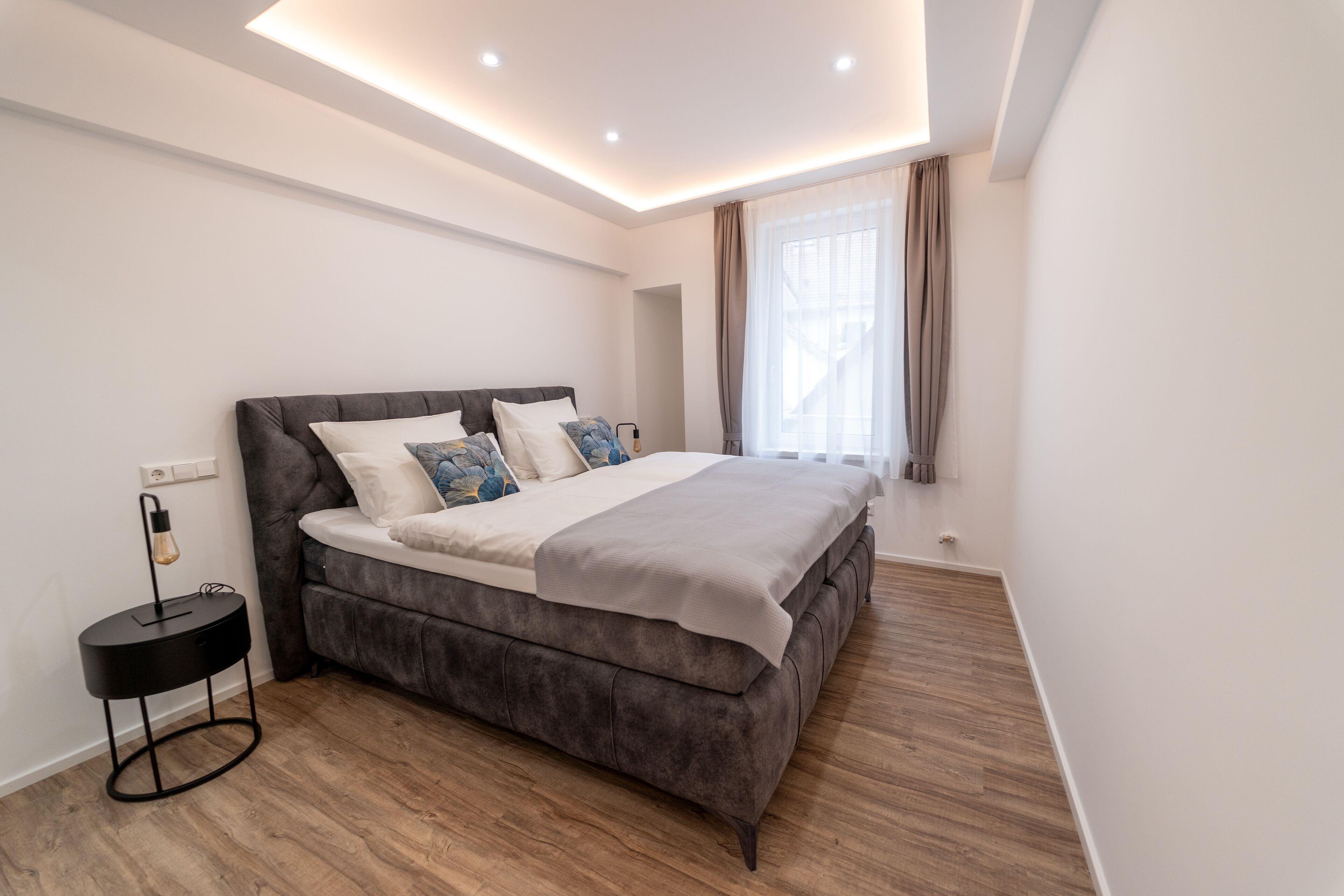 Une chambre moderne avec un grand lit, une table de chevet et une fenêtre avec des rideaux.