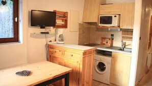 Una cocina compacta con armarios de madera, un microondas, una lavadora y una pequeña mesa.
