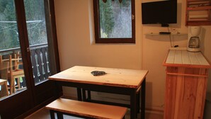 Una habitación pequeña con una mesa de madera y un banco, un televisor montado en la pared y una cafetera en un estante.