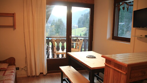 Una habitación con una mesa de madera, un banco y vistas a un balcón con sillas.