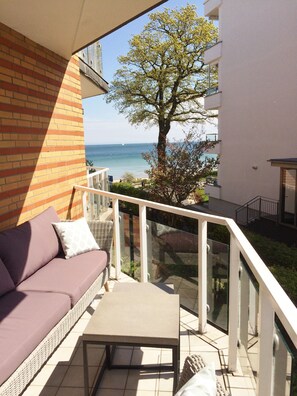 Un balcón con sofá y mesa, con vistas a un árbol y al mar.
