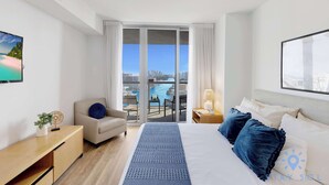 Ein Hotelzimmer mit Bett, Schreibtisch, Stuhl, Blick auf die Stadt und einem Balkon mit Tisch und Stühlen.