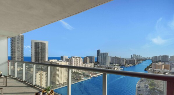 A balcony with a city view, a table with a plant, and a clear blue sky. - Stylish Beach Apartment with Pool (Hallandale Beach)