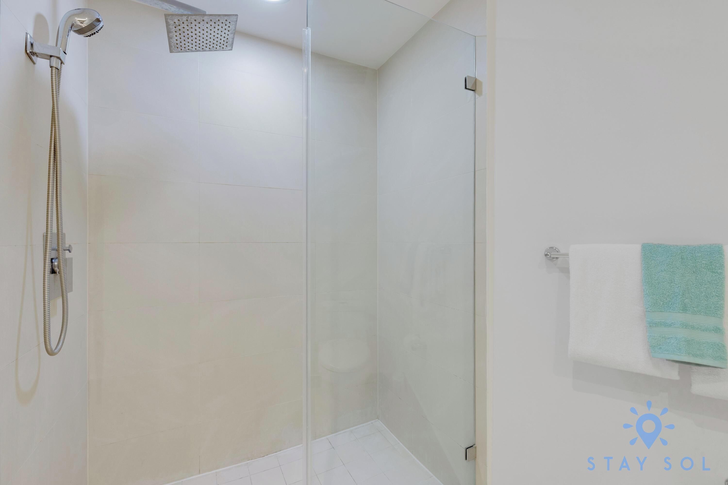A glass-enclosed shower area with a handheld showerhead and a wall-mounted showerhead.
