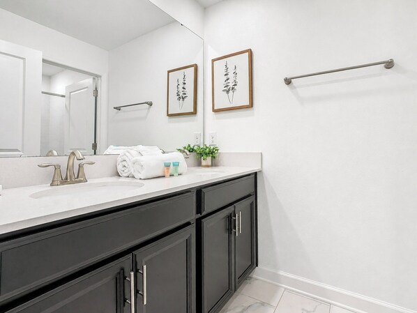 A modern bathroom with a white sink, dark cabinets, a large mirror, and two framed botanical prints on the wall.