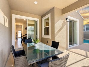 A glass-top dining table with wicker chairs, a potted plant, and a view of a swimming pool through a sliding glass door.