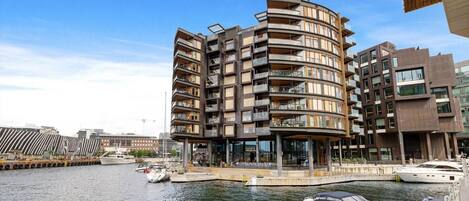 A waterfront building with multiple balconies, a dock with boats, and a clear sky.