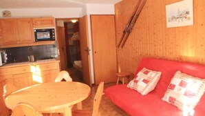 A compact living space with a kitchenette, a dining area, and a red sofa with patterned cushions. - Gelinote Chalet for 4 People (Chatel)