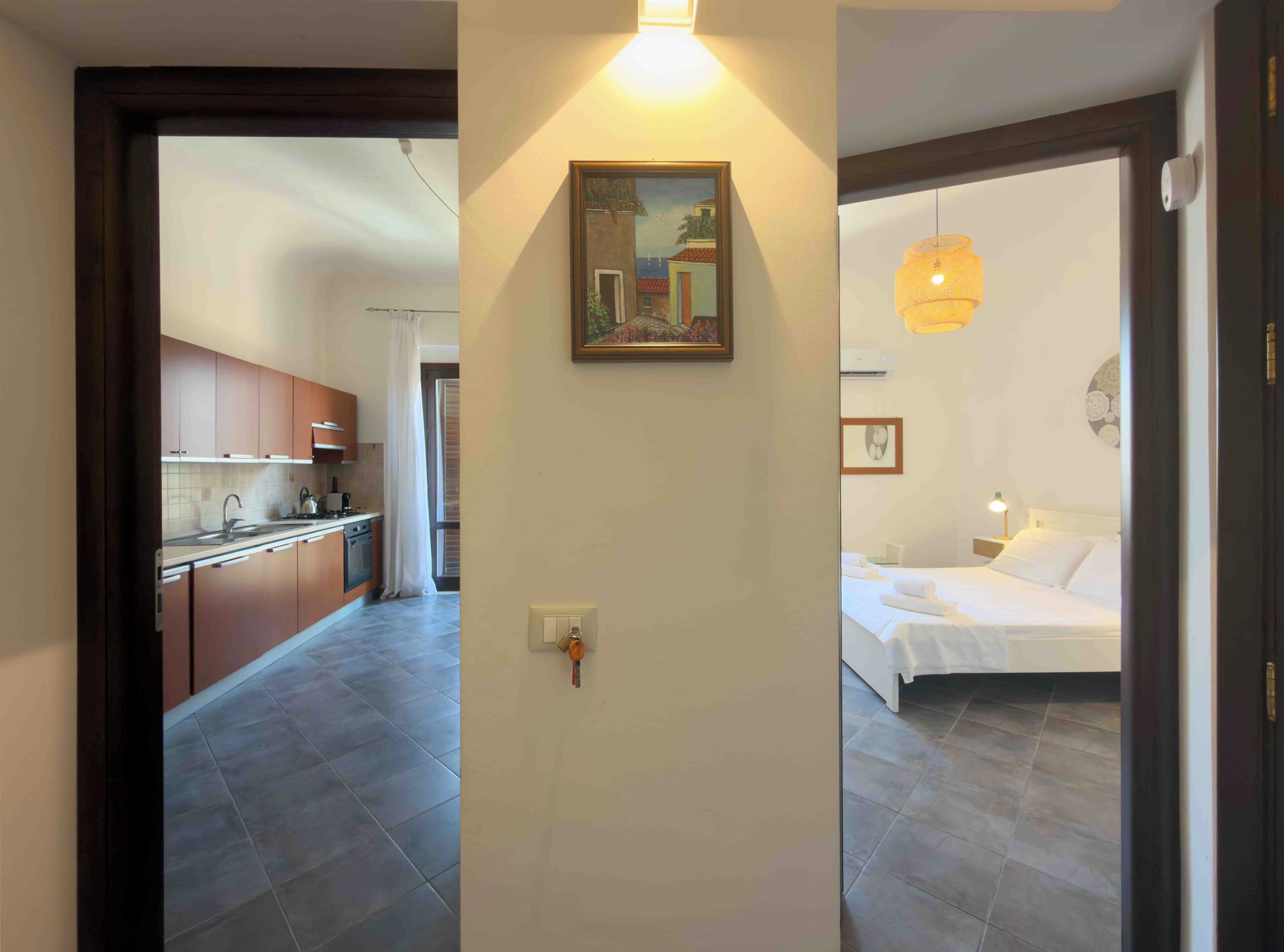 Een moderne keuken met een eethoek, een slaapkamer met een bed en nachtkastje, en een schilderij aan de muur.