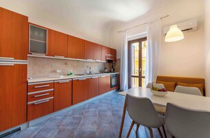 Una cocina moderna con armarios de madera, salpicadero de azulejos, comedor con mesa y sillas, e iluminación colgante.