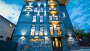 Un immeuble à plusieurs étages, doté d’une façade en pierre, de nombreux balcons et d’une entrée imposante avec une porte décorative.
