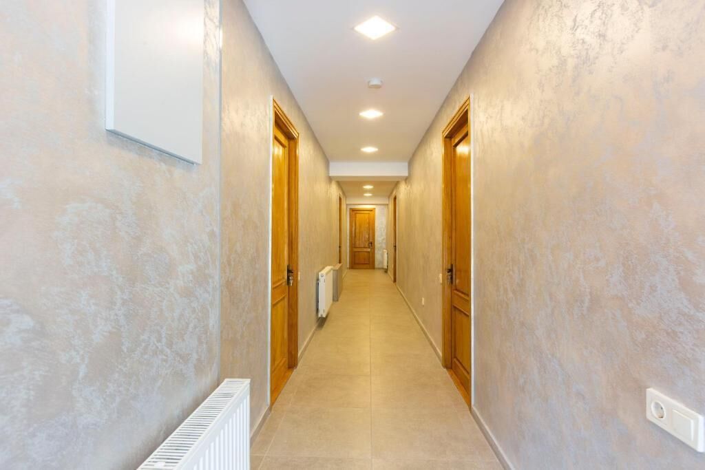 Un pasillo con paredes color beige y puertas de madera que conduce a una habitación con un radiador y un interruptor de luz en la pared.