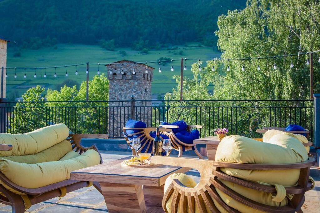 An outdoor seating area with wooden furniture and a view of a stone tower and greenery.