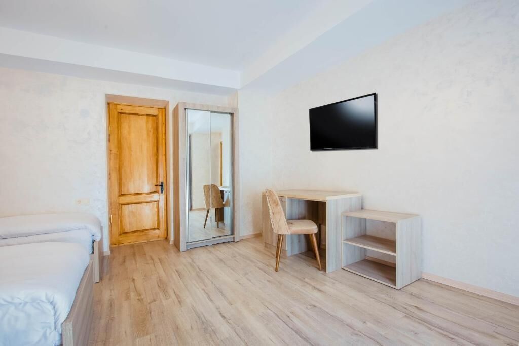 A room with a bed, a desk with a chair, a television, and a sliding door.