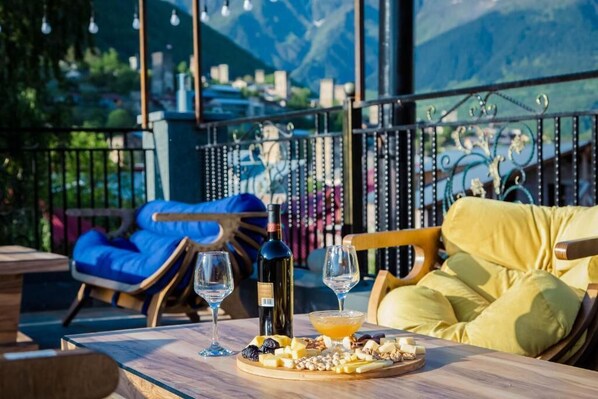 Une terrasse avec une table dressée pour un repas, comprenant du fromage, des noix et une bouteille de vin.