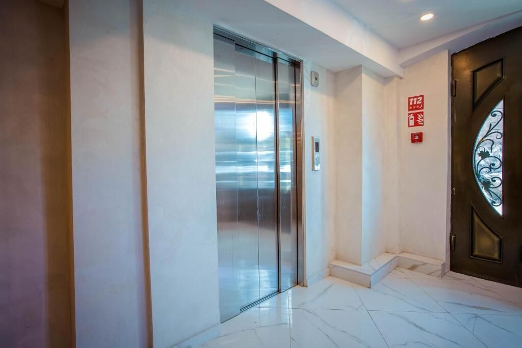 Een moderne lift met glazen deur, een brandmeldingsbord en een decoratieve deur met een glaspaneel.