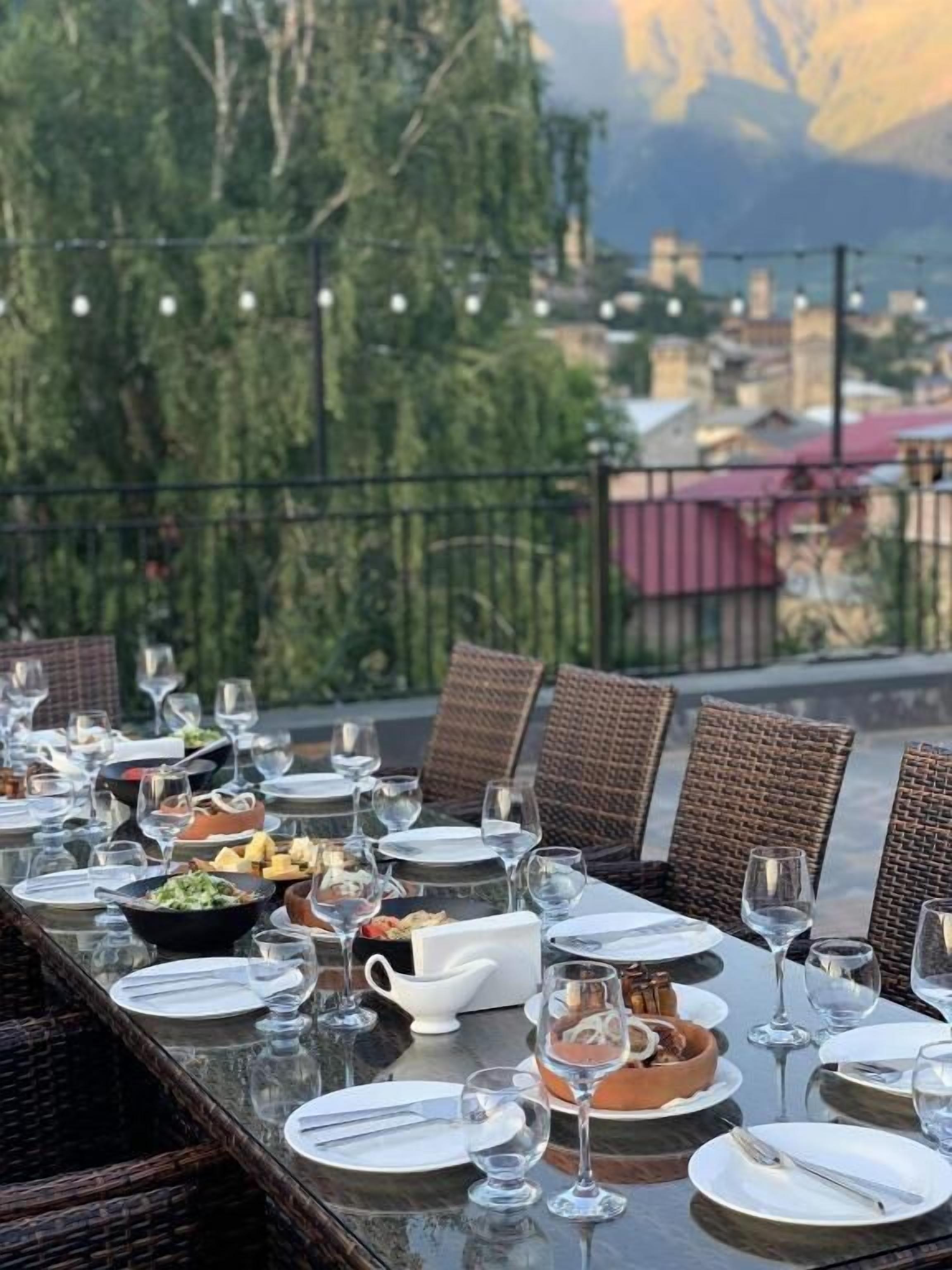 Tavola imbandita per un pasto, con diversi piatti e bicchieri di vino, con vista su un paesaggio montuoso.