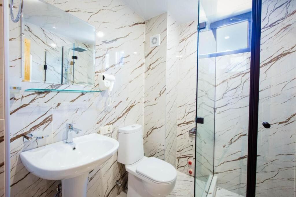 Baño con pared de mármol, cabina de ducha de vidrio, lavamanos e inodoro.