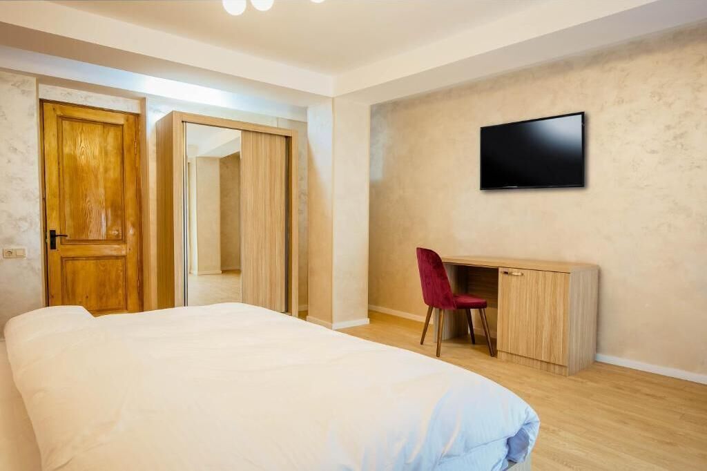 A bedroom with a bed, a desk with a chair, a television, and a wardrobe.