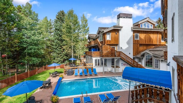A backyard with a swimming pool, lounge chairs, and a wooden deck. - Chateau Christian | 220 - 2 Bedroom Gold (Vail)