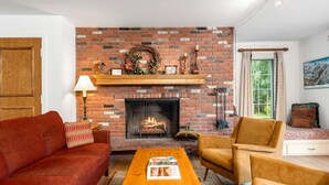 A living room with a brick fireplace, a wooden coffee table, a red sofa, and a brown armchair. - Chateau Christian | 220 - 2 Bedroom Gold (Vail)