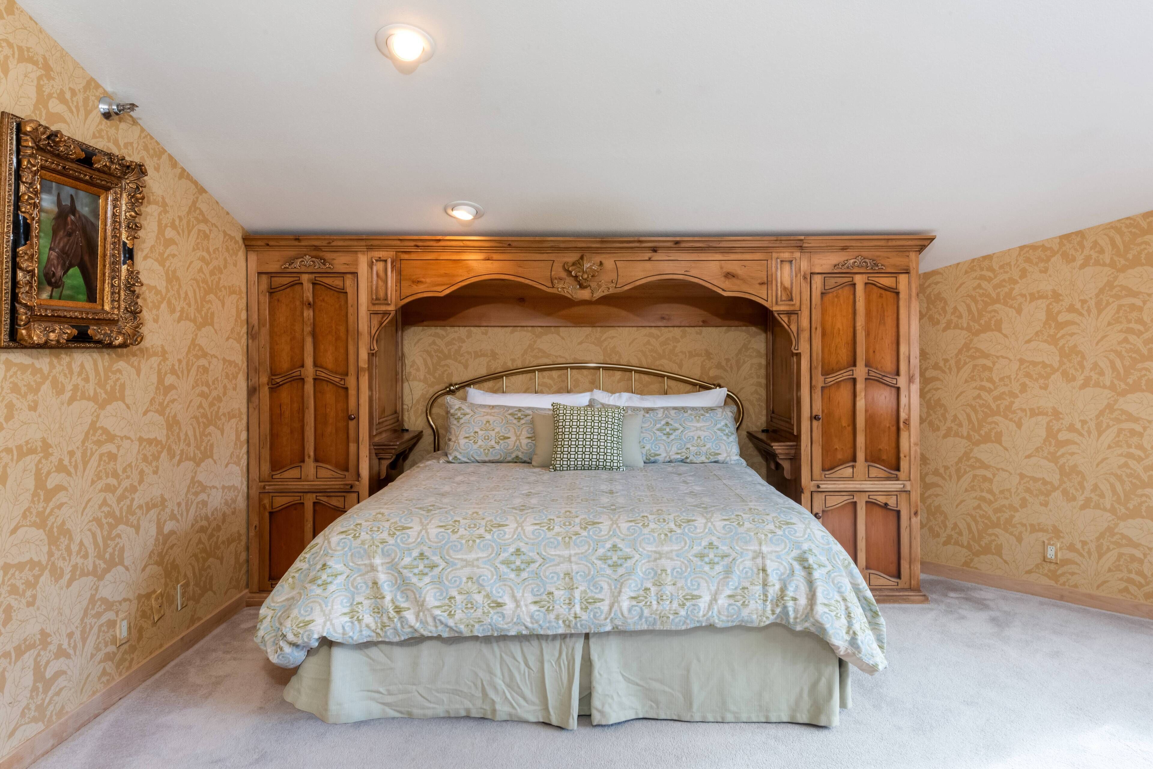A bedroom with a large bed, wooden headboard, and patterned wallpaper.
