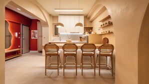 A modern kitchen with a central island, four wicker chairs, and pendant lighting. - Gaia Nest 1-bedroom apartment in Piraeus (Pireas)