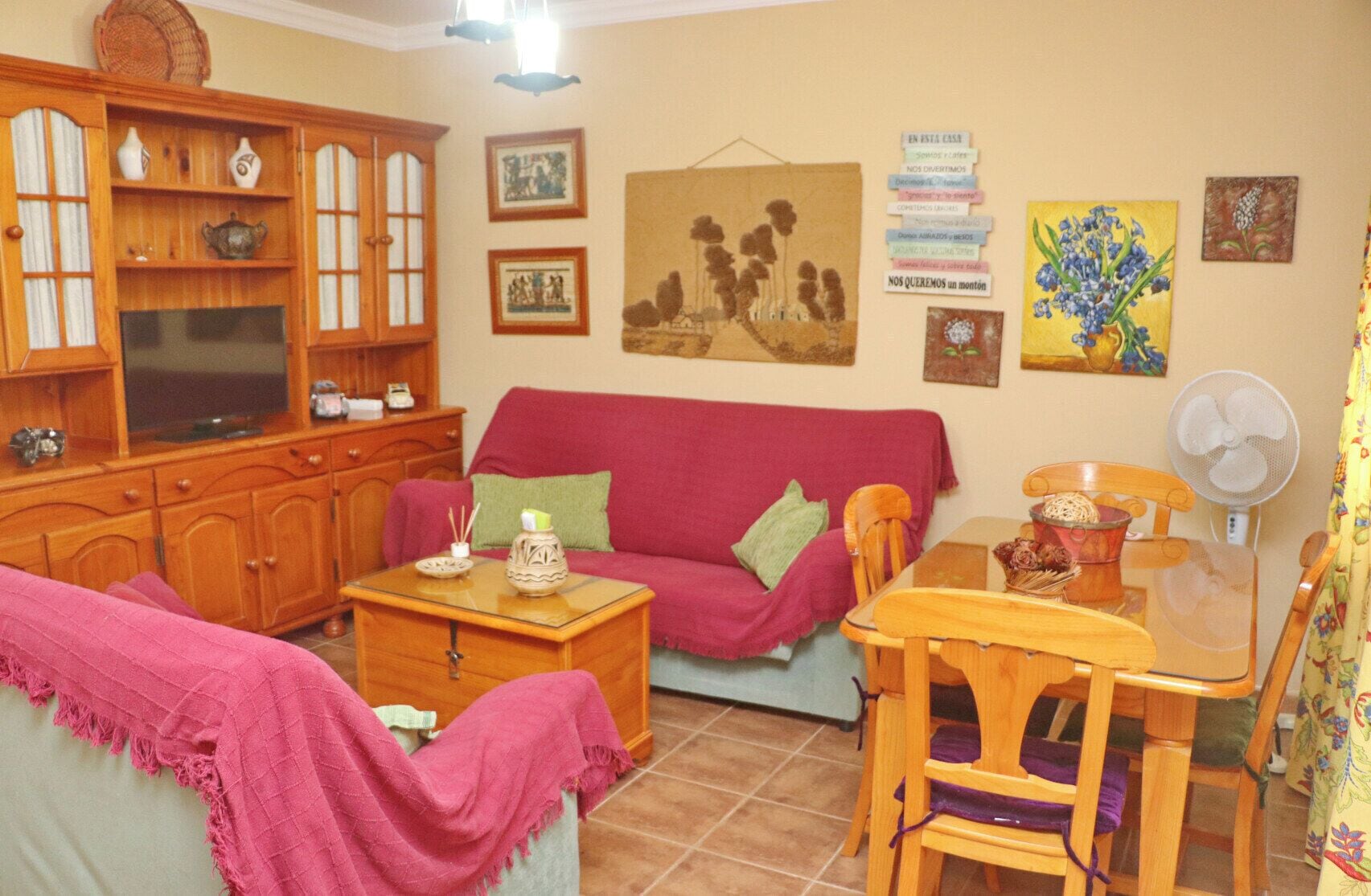 Uma sala de estar acolhedora com sofá vermelho, armários de madeira, mesa de centro de vidro e mesa de jantar com cadeiras.