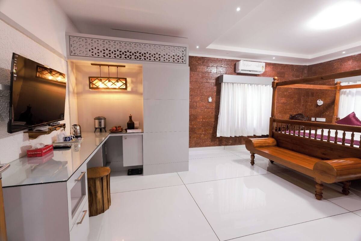 A modern hotel room with a flat-screen TV, a small kitchenette, a wooden bench, and a decorative wall panel.
