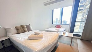 Et moderne hotelværelse med en stor seng, en mindre seng, et skrivebord og et vindue med udsigt over byen.