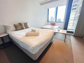 A modern hotel room with a large bed, a smaller bed, a desk, and a window with a city view. - Cozy Studio Apt Near Southern Cross & City Views (Melbourne)