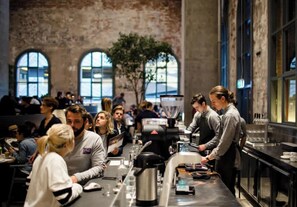 A busy cafe with a rustic brick wall, large windows, and a coffee machine. - Cozy Studio Apt Near Southern Cross & City Views (Melbourne)