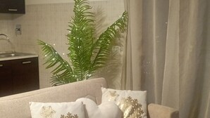 Una sala de estar con un sofá color beige, almohadones decorativos, una planta en maceta y un televisor montado en la pared.