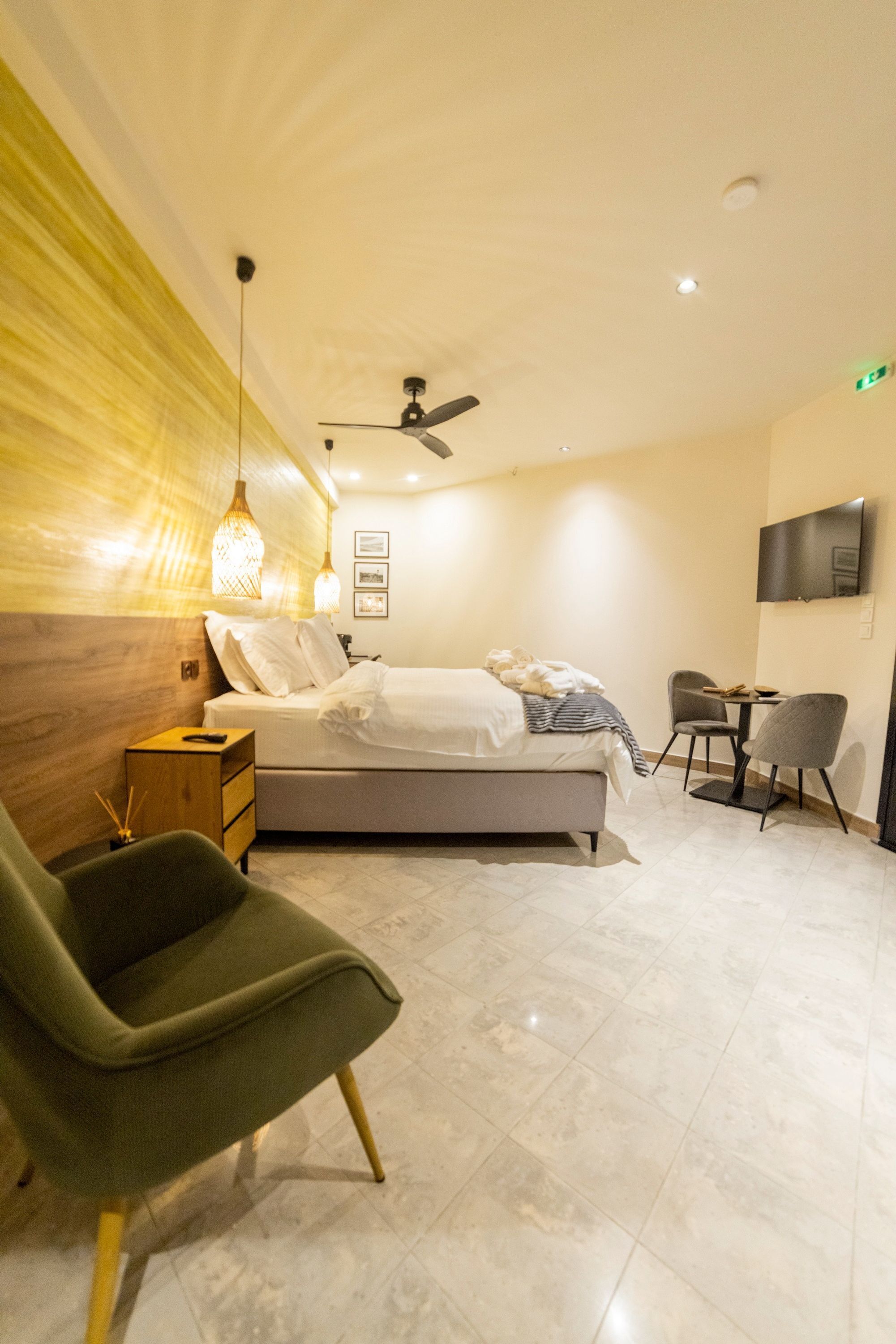 A modern hotel room with a bed, bedside table, lamp, chair, and a TV on the wall.