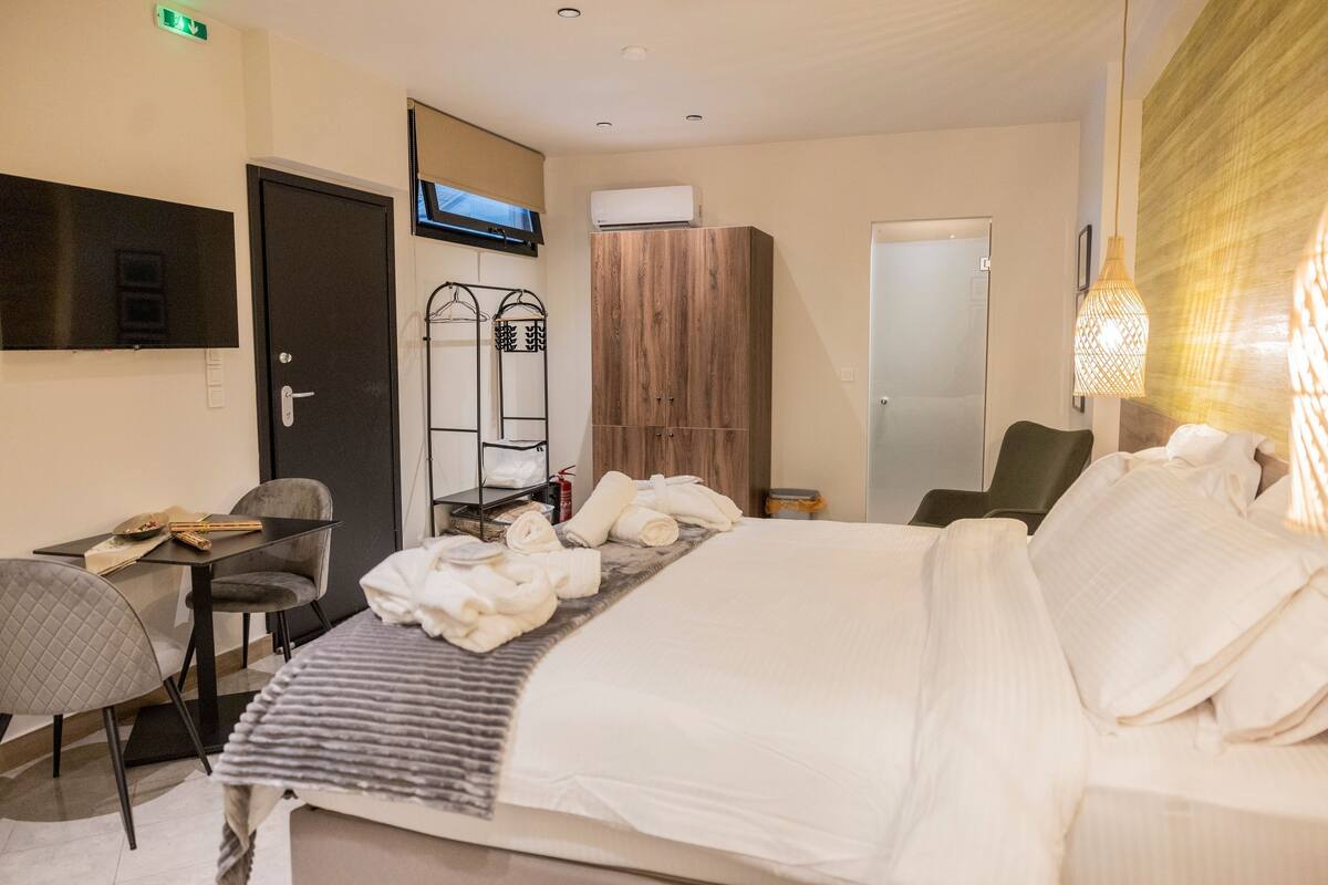 A hotel room with a bed, a desk with a chair, a wardrobe, a television, and a hanging light fixture.