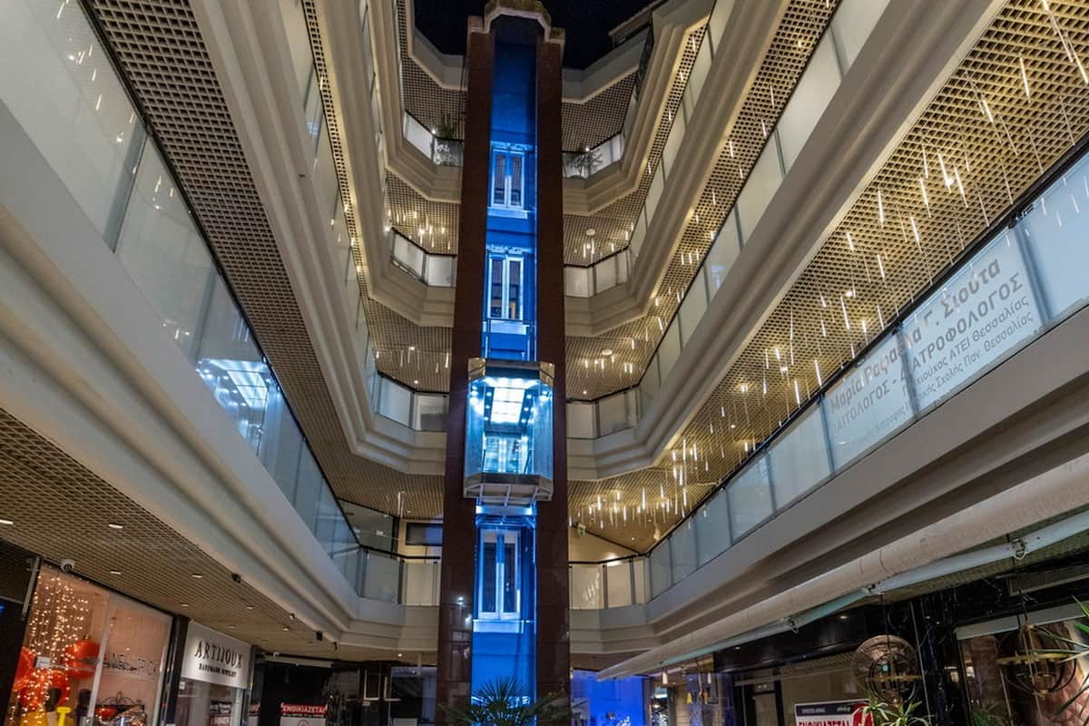 A multi-level atrium with a central illuminated column, glass railings, and various shops on the ground floor.