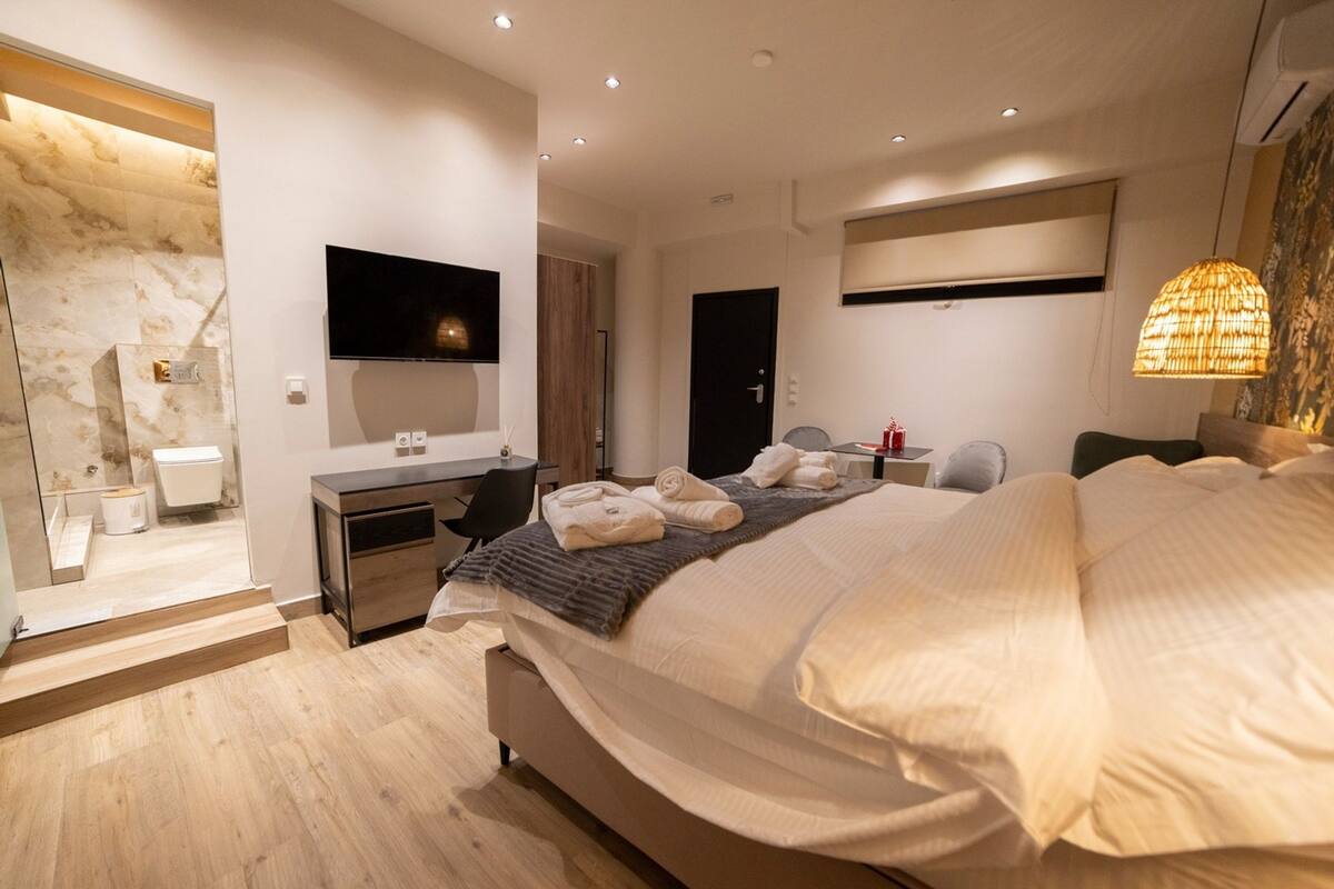 A modern hotel room with a large bed, a desk, a flat-screen TV, and a bathroom with a marble wall.