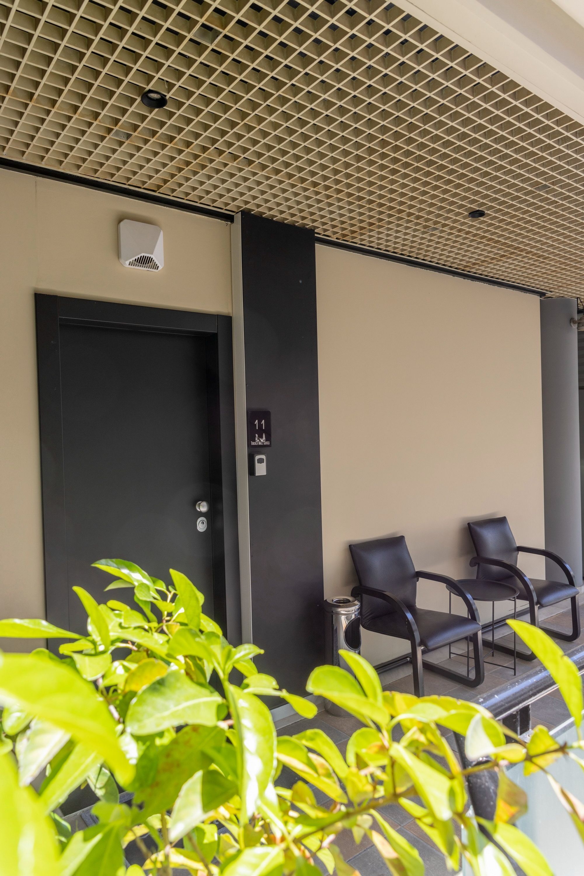 A modern hotel lobby with a black door, a seating area with black chairs, and a ceiling with a grid pattern.