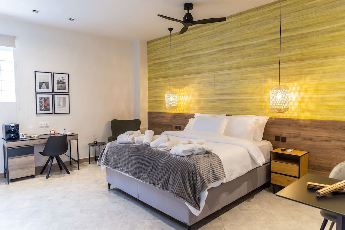A modern hotel room with a bed, desk, chair, and a wall-mounted ceiling fan.