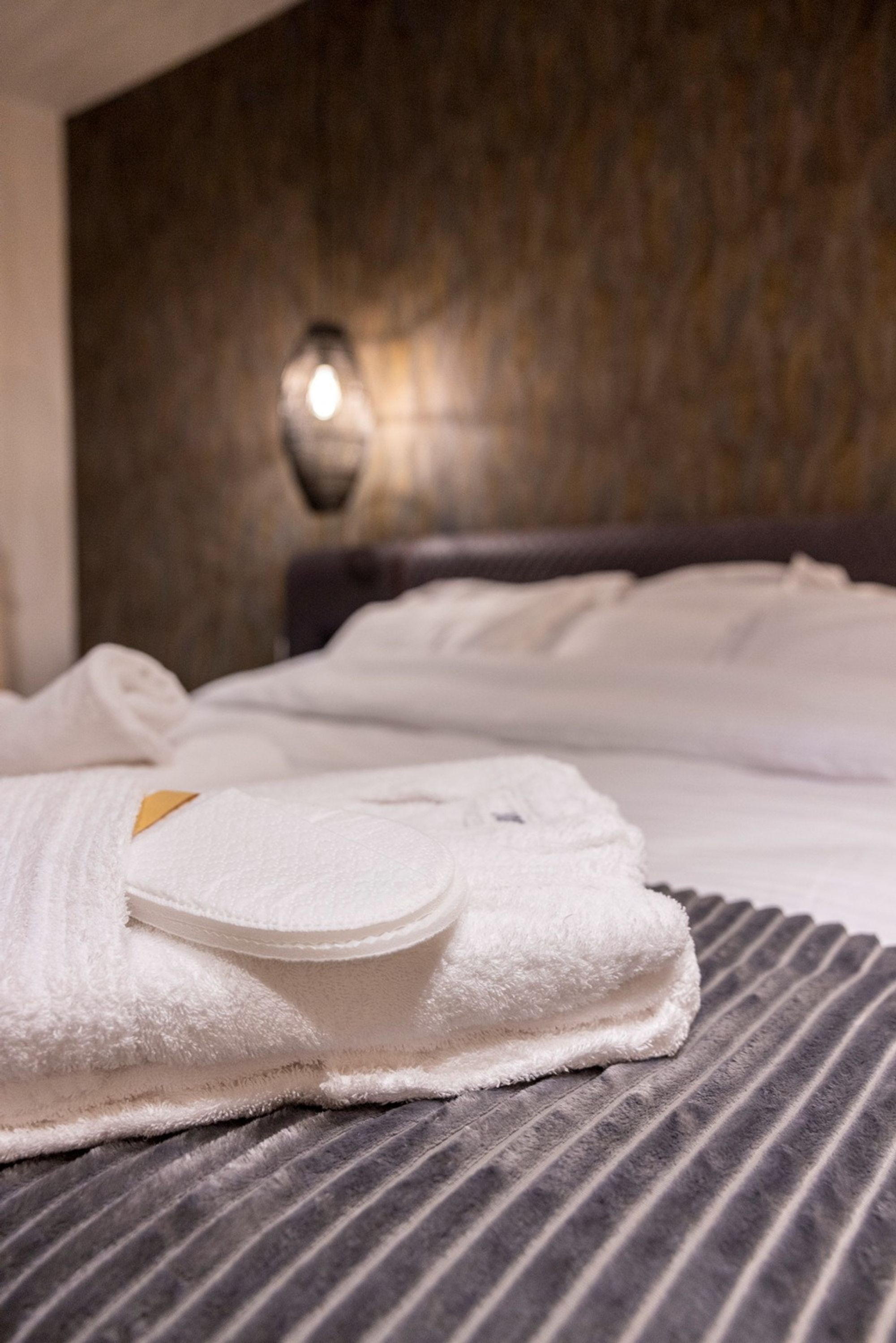 A neatly made bed with a folded white towel and a small brown pillow on a striped gray bedspread.