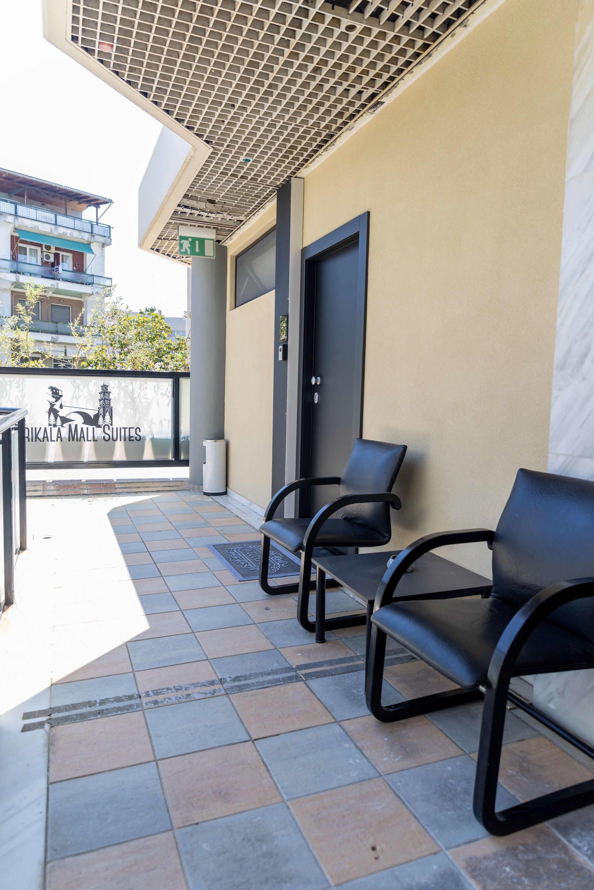 A hotel exterior with a tiled patio, black chairs, a door, and a sign for Rikala Mall Suites.
