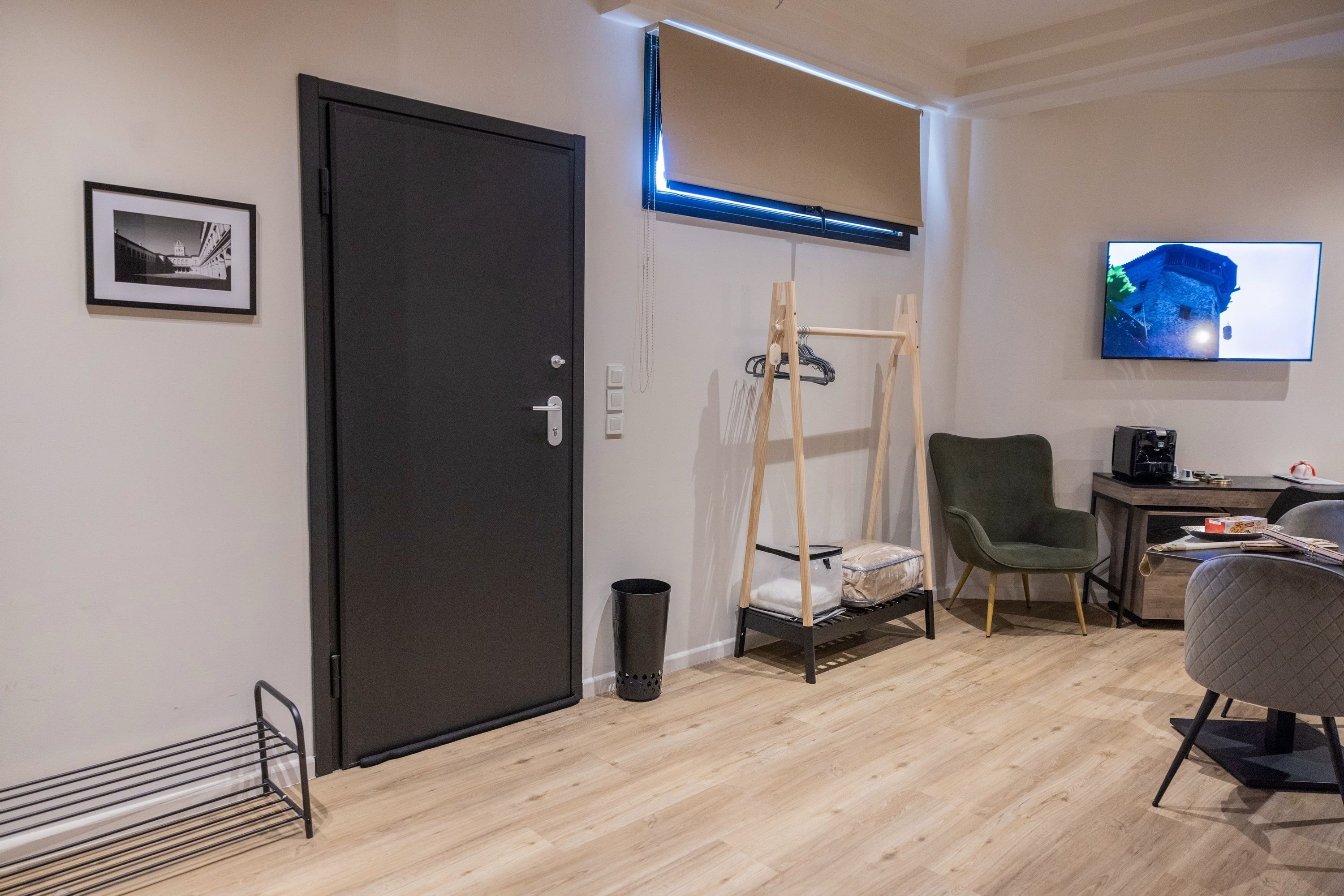 A modern room with a black door, a bed with a canopy, a green chair, a desk with a computer, and a TV mounted on the wall.