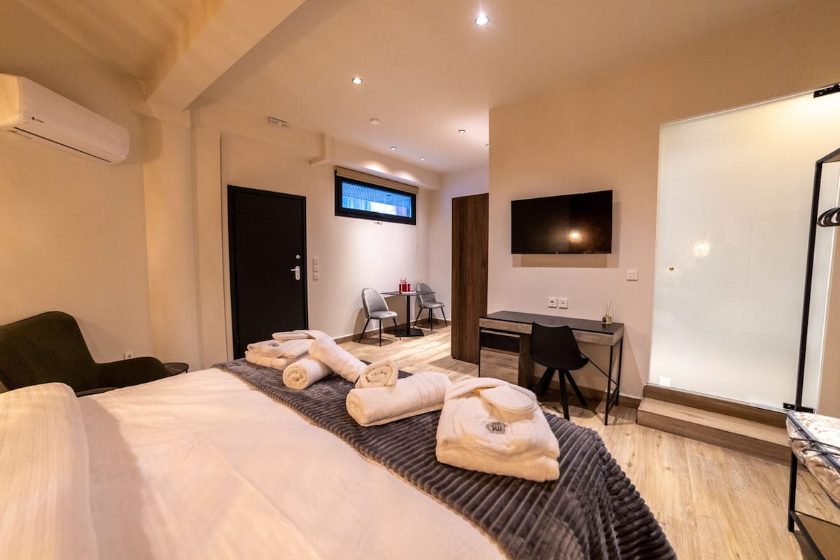 A hotel room with a bed, a desk, a TV, and a shower area.