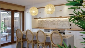 Une cuisine moderne avec des meubles blancs, un pare-feu en pierre et un coin repas doté de chaises en osier.