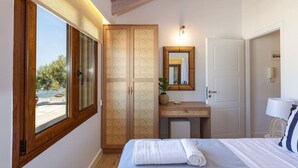 Une chambre à coucher comprenant un lit, une coiffeuse avec un miroir, une armoire et une fenêtre donnant sur un paysage verdoyant.