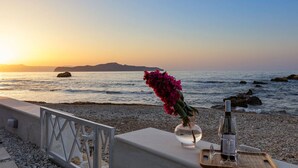 Une terrasse en bord de mer avec une table dressée pour deux personnes, agrémentée d’un vase de fleurs et d’une bouteille de vin.
