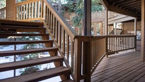 Una terraza de madera con una escalera que conduce a un nivel superior, rodeada de árboles.
